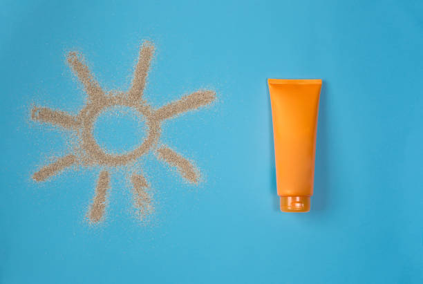 Sun drawn by the sand on blue background. Sunscreen on blue background. Top view. stock photo