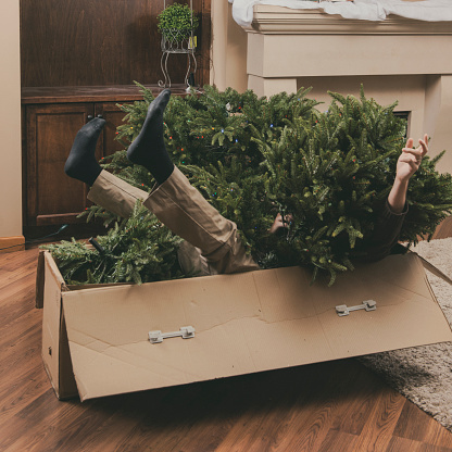 Man trapped by artificial Christmas tree - metaphor for stress of the holiday season
