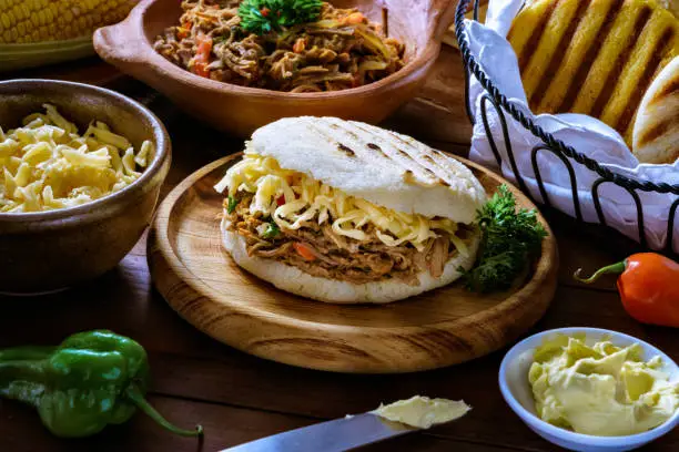Venezuelan traditional food (Arepa Pelua) or white corn Arepa with shredded cheese and meat. Ingredients on a table in a rustic kitchen. Corn flour, cheese, corn cobs, butter, water and salt. Arepas, or corn bread, is a main meal in the Venezuelan Culture and cuisine.