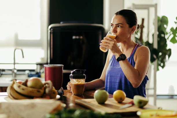 jeune femme athlétique buvant le smoothie de fruit dans la cuisine. - routine foods and drinks clothing household equipment photos et images de collection