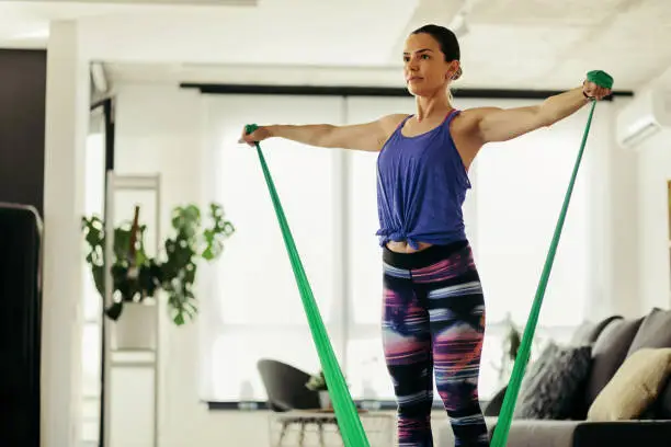 Young female athlete using resistance band while working out in the living room.