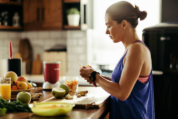 donna atletica che affetta frutta mentre prepara frullato in cucina. - smoothie fruit juice healthy eating foto e immagini stock