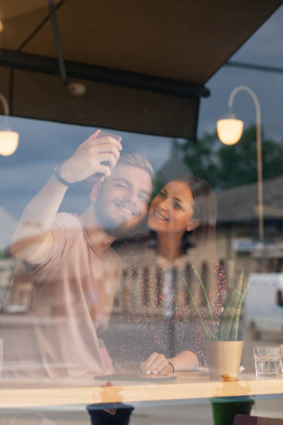 istock two smiling friends, making a selfie in a cafe. Shot thought a window with reflections (street / city life). 1161292167