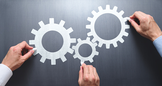 Businessmen drawing gears on chalkboard.