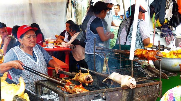 Cuenca, Ecuador - March 31, 2019: Vendor woman prepares cuy or roasted guinea pig - traditional delicious food of South America at food festival in Cuenca. There are street restaurant and a few people eating