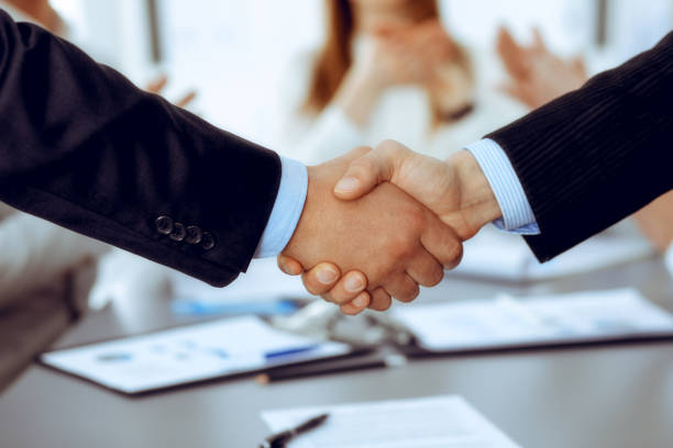 istock Business people shaking hands at meeting while theirs colleagues clapping and applauding. Group of unknown businessmen and women in modern white office. Success teamwork, partnership and handshake concept 1161321656