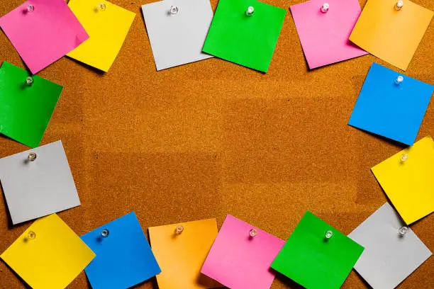 Photo of Corkboard/Bulletin Board bordered completely by very disorderly multicolored sticky type square notes.  The notes are all blank and easily edited with copy and the center of the image is completely open for copywriting.