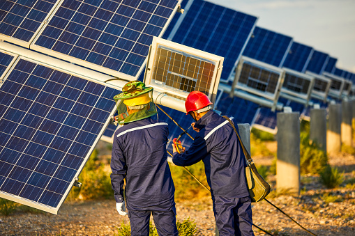 In the sunset, Asian workers are checking solar photovoltaic panels, outdoor wind and sand landforms