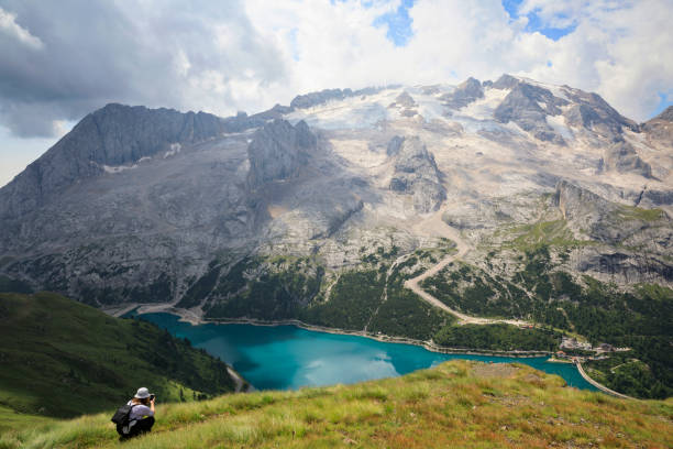 Senior woman enjoying, taking photographs with her smartphone. Beautiful view of lake Fedaia and Marmolada mountain from resting point on path from Fedaia pass to pass Pordoi in Dolomites, Northern Italy. Summer on the mountain Arabba. mujer mayor disfrutando, tomando fotografías con su teléfono inteligente. hermosa vista del lago fedaia y la montaña marmolada desde el punto de descanso en el camino de fedaia pasar para pasar pordoi en dolomitas, norte de italia. verano en la montañ