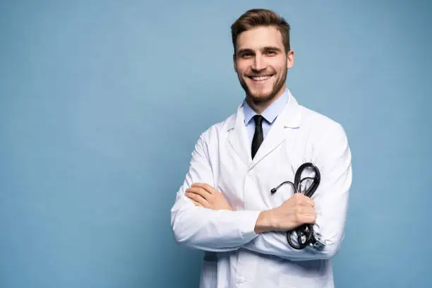 Photo of Portrait of confident young medical doctor on blue background.