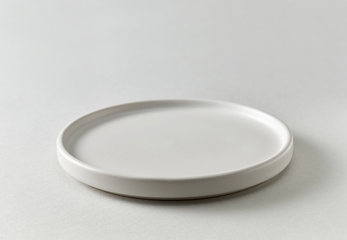 empty white plate on light grey paper background, selective focus