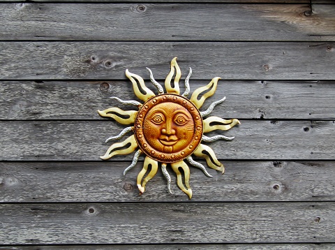 Sun face plaque hanging on a wooden panel wall
