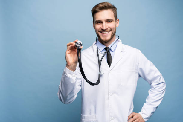 istock Handsome young medic holding a stethoscope, isolated over light blue. 1161339917