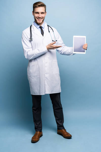istock Full length of friendly doctor presenting empty digital tablet screen. Isolated on light blue. 1161342126