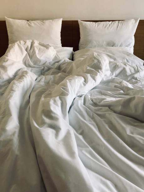 A messy bed with comforter and pillows - stock photo