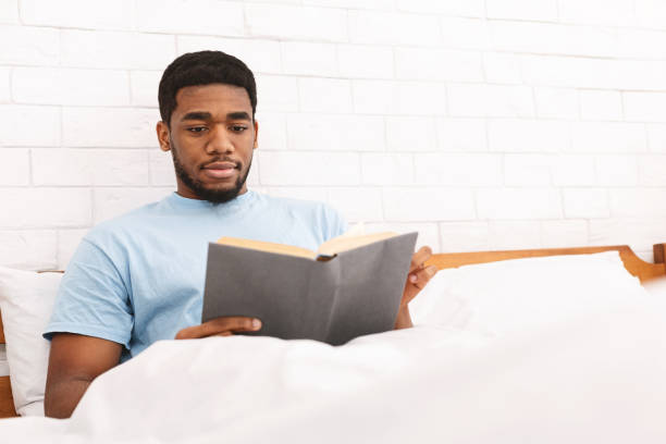 istock Pensive young guy reading book in bed 1161346457