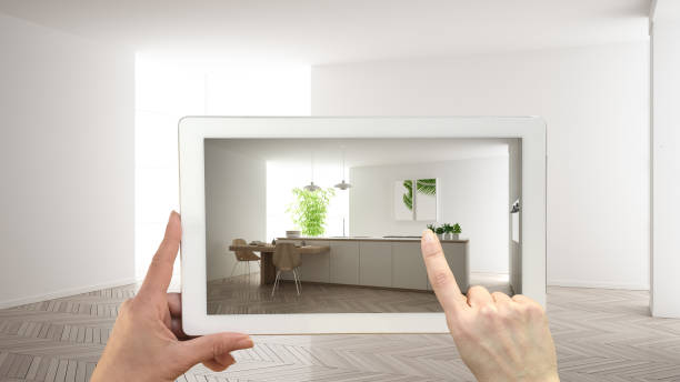 istock Augmented reality concept. Hand holding tablet with AR application used to simulate furniture and design products in empty interior with parquet floor, modern white kitchen 1161346821