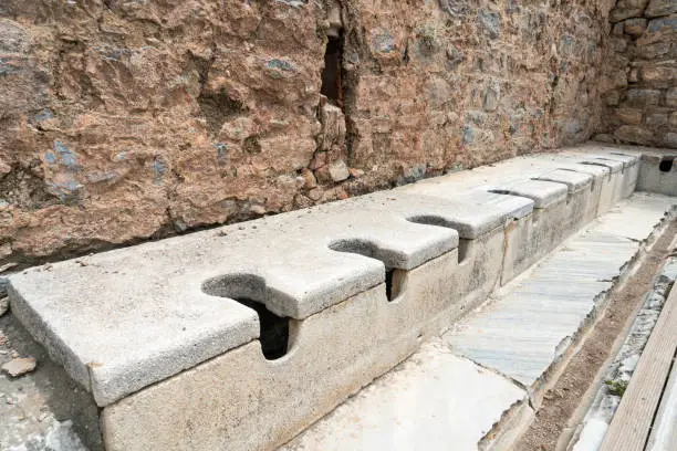 Public multi seat toilet marble stone and rock at spectacular antique ruins in Ephesus at Selcuk Izmir, Turkey. Historical Ancient Greek toilet system stone.