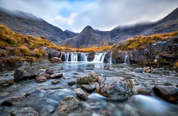 Fairy Pools, Glen Brittle, Isle of Skye, Scotland, UK Waterfall in the Fairy Pools, Glen Brittle, Isle of Skye, Scotland, UK. On a gray day in the fall you see the water flowing along the rocks with in the background the famous mountain with the crack in the middle from top to bottom falling water flowing water stock pictures, royalty-free photos & images