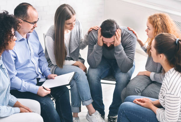Depressed man with alcoholism problem sitting in rehab center Depressed man with alcoholism problem sitting in rehab center, group supporting him, free space alcoholics anonymous photos stock pictures, royalty-free photos & images