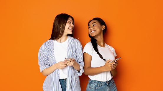 Teen girls looking at each other and using cellphones, orange background