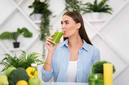 Healthy lifestyle. Woman drinking smoothie, sitting in kitchen, having lunch