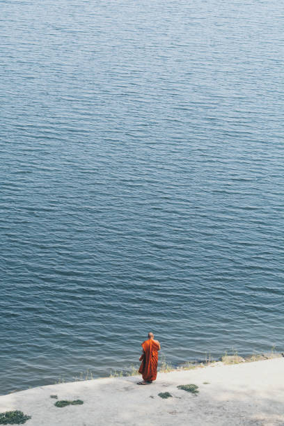Bagan, Myanmar - March 2019: Burmese Buddhist monk in orange robe standing on the banks of Irrawaddy river in Bagan, Myanmar.