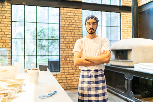 Portrait of pizzaiolo standing with arms crossed in front of pizza oven