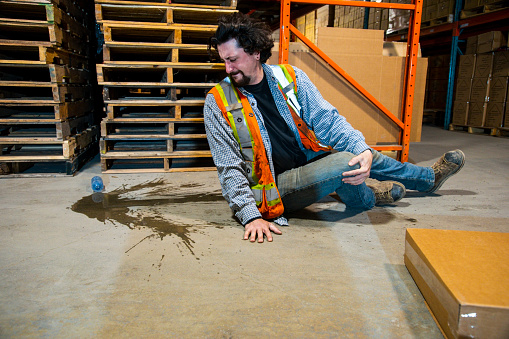 An industrial, warehouse, workplace safety topic.  An employee risks injury by slipping on a plastic water bottle.  Slips, trips and falls are major contributors to safety incidents in distribution centers, and factories.