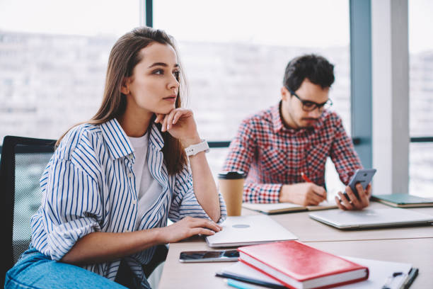 istock Contemplative woman looking away thinking about idea for startup sitting at desktop next to concentrated male colleague writing and using smartphone, professional employees during working process 1161359878