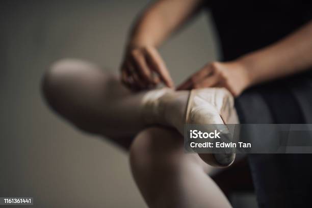 A Young Asian Chinese Female Ballet Dancer Getting Ready Tying Her Shoelace Before Practising Her Ballet Dance In Ballet Studio Stock Photo - Download Image Now