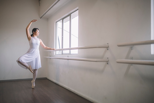 an asian chinese female teenager ballet dancer practising in ballet studio during day time