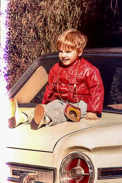 Vintage photo of a cute kid sitting on a vintage car.
