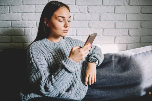 istock Pensive female using cellular for banking online transfering money via application, brunette female reading news from social networks browsing web page on smartphone sitting on sofa during break 1161370432