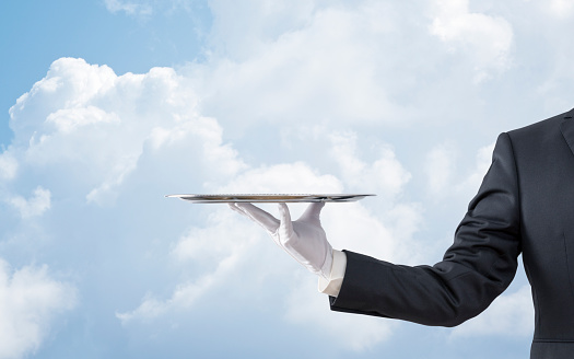 Waiter holding empty silver tray over blue sky