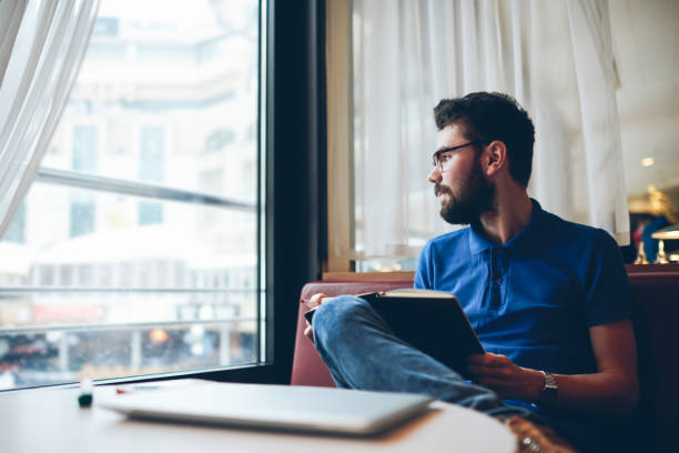 istock Young pensive male journalist thinking about creating article while thoughtful looking at cafe window, clever contemplative hipster guy learning at university campus while waiting friend on coach 1161379627