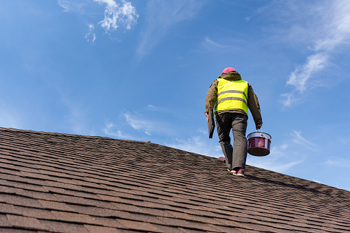 Trabajador irreconocible y cualificado en uniforme de pie sobre el techo de teja de la nueva casa en construcción con equipo e instrumento photo
