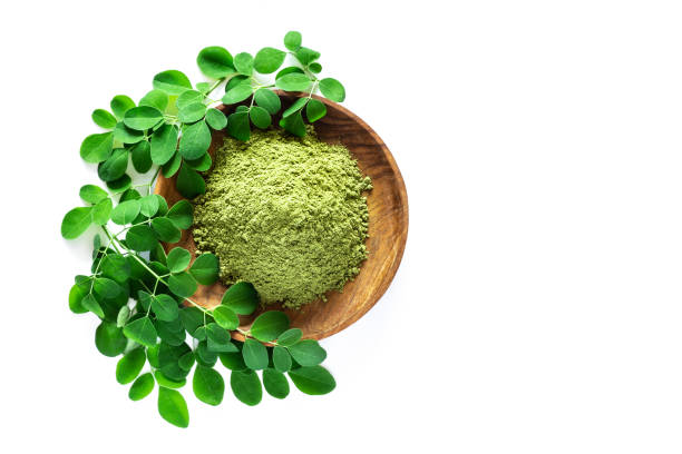 Moringa powder (Moringa Oleifera) in wooden bowl with original fresh Moringa leaves isolated on white background. Moringa powder (Moringa Oleifera) in wooden bowl with original fresh Moringa leaves isolated on white background. Healthy product, superfood, vitamin. Top view. moringa leaves stock pictures, royalty-free photos & images