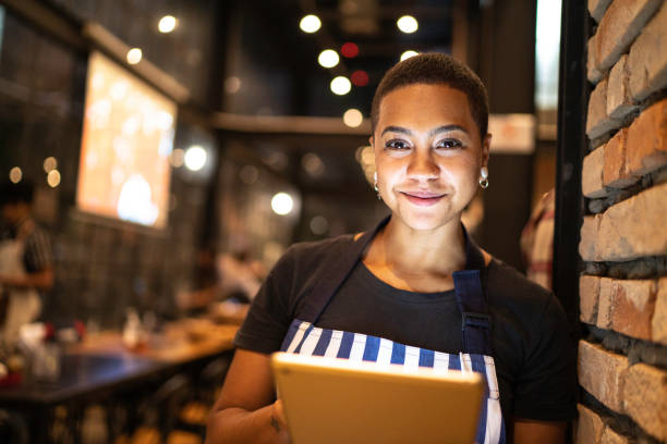 Portrait of young woman looking at camera and holding a digital tablet at restaurant Portrait of young woman looking at camera and holding a digital tablet at restaurant pizzeria stock pictures, royalty-free photos & images
