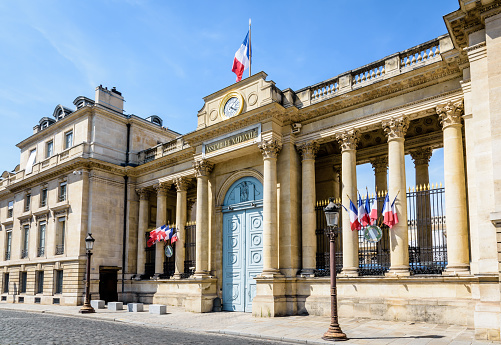 Southern entrance of the Palais Bourbon, seat of the French National Assembly in Paris, France, decked with french flags on a sunny summer day.