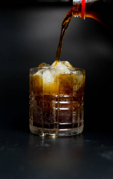 istock Pouring cola from bottle into glass with ice cubes on table 1161397813