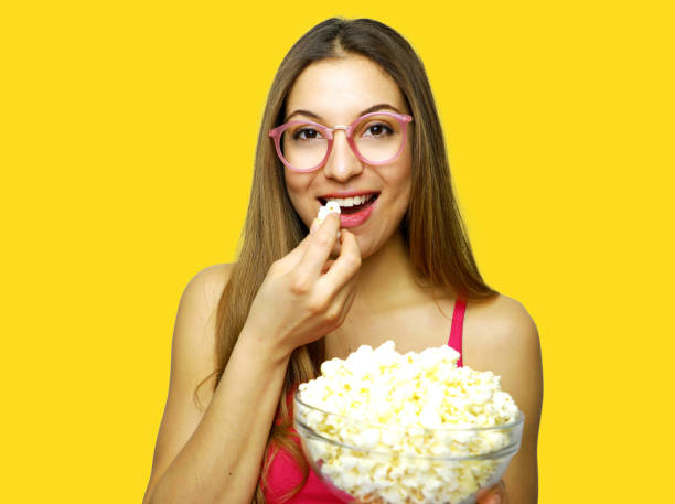 mulher nova que tem pipoca contra fundo amarelo - popcorn snack bowl isolated - fotografias e filmes do acervo