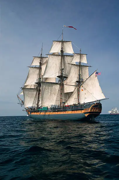 Vintage frigate Sailing Ship at Sea under full sail with tall ships in the background.