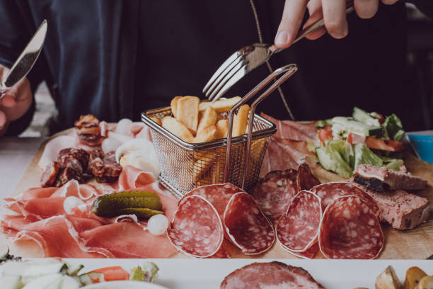 manos macho sosteniendo un tenedor sobre el plato de carnes frías, enfoque selectivo. - grasa saturada fotografías e imágenes de stock