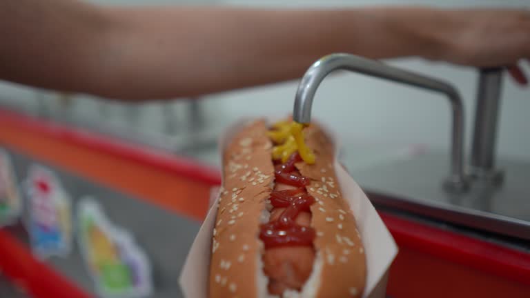 Unrecognizable customer at the cinema adding mustard to a hot dog