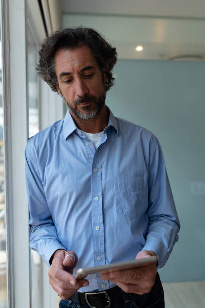 istock Businessman working on digital tablet while standing near window in office 1161409097