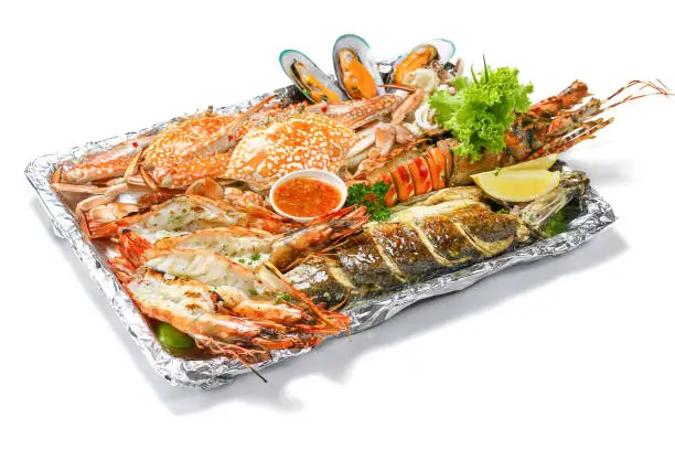 Grilled Mixed Seafoods platter Set contain Lobsters Fish Blue Clabs Big Shrimps Mussels Clams Calamari Squids with pieces of lemon & vegetables isolated on white background, High Angle Top side view.