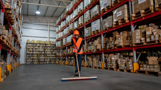 istock Blue collar worker sweeping a distribution warehouse with an industrial broom 1161410984