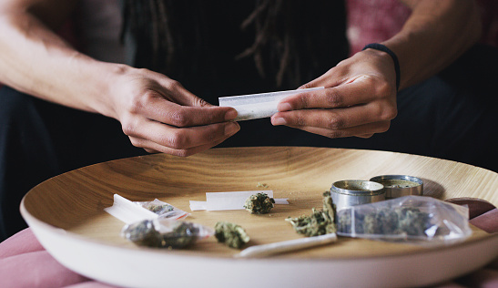 Cropped shot of a man rolling a marijuana joint at home