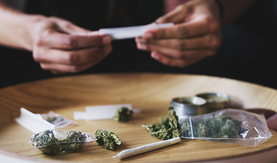 Cropped shot of a man rolling a marijuana joint at home